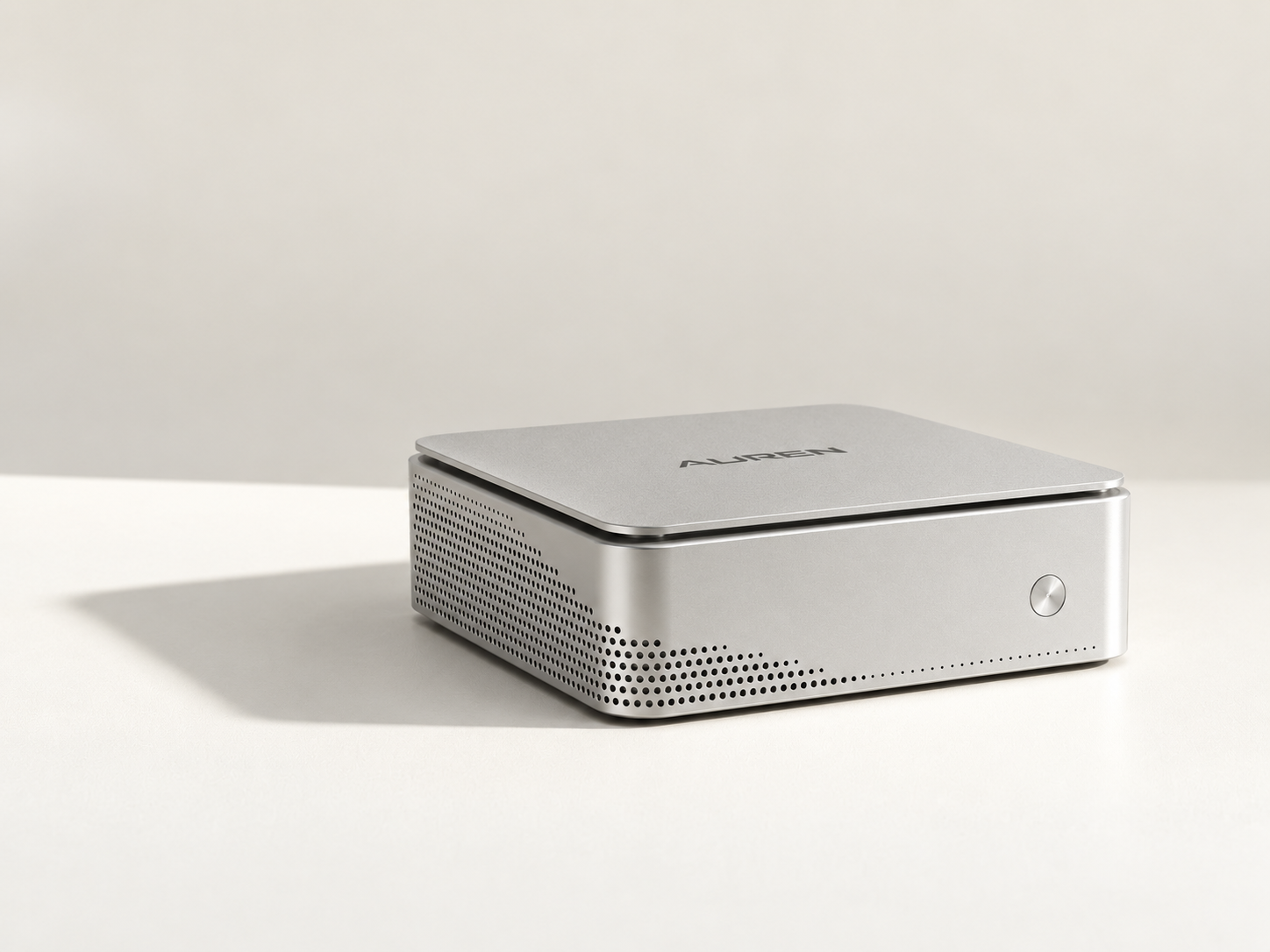 Auren One, a compact brushed aluminium desktop computer, on a warm off-white surface